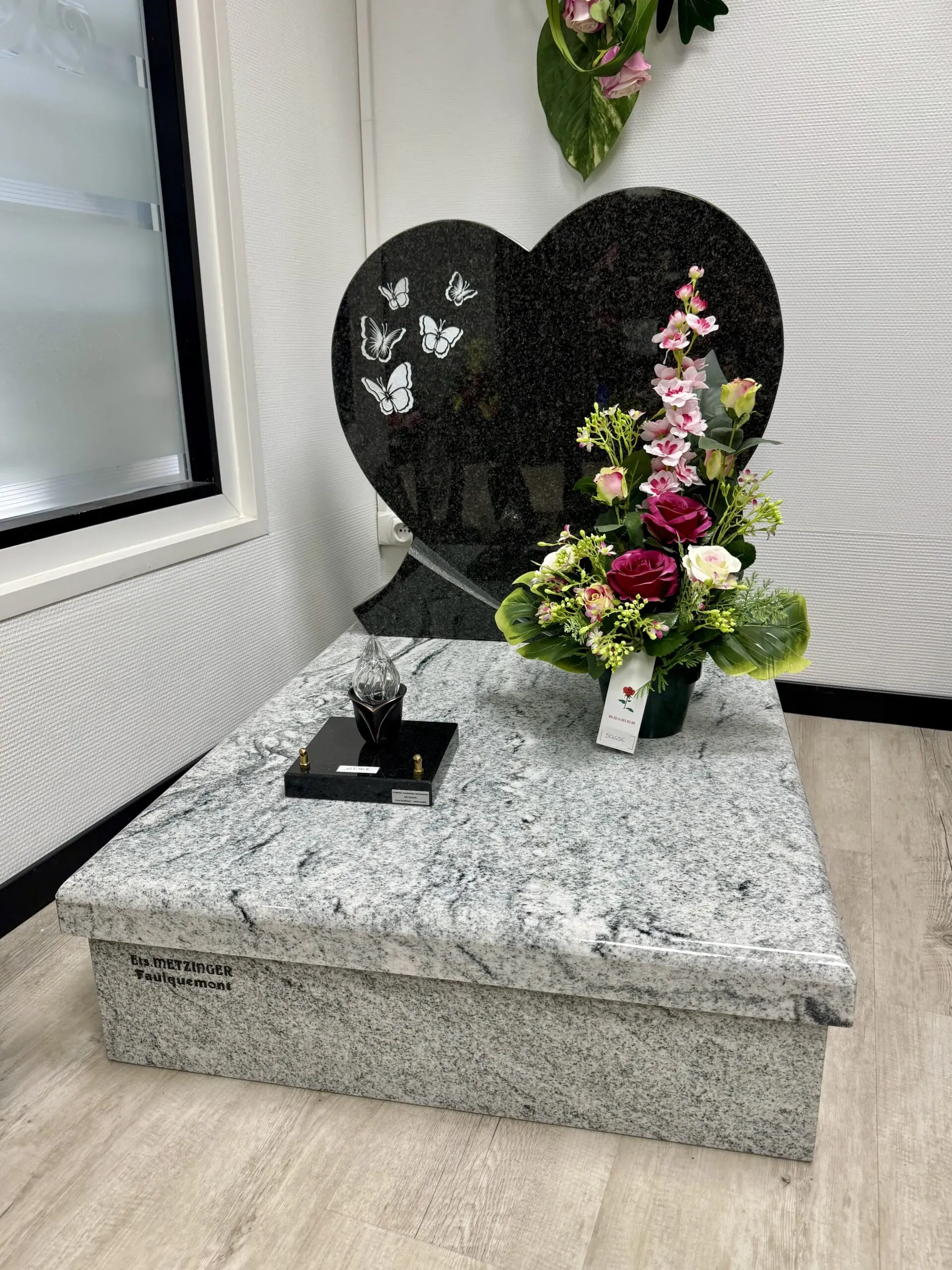 Monument funéraire en granit sombre en forme de cœur décoré d'un bouquet de fleurs.