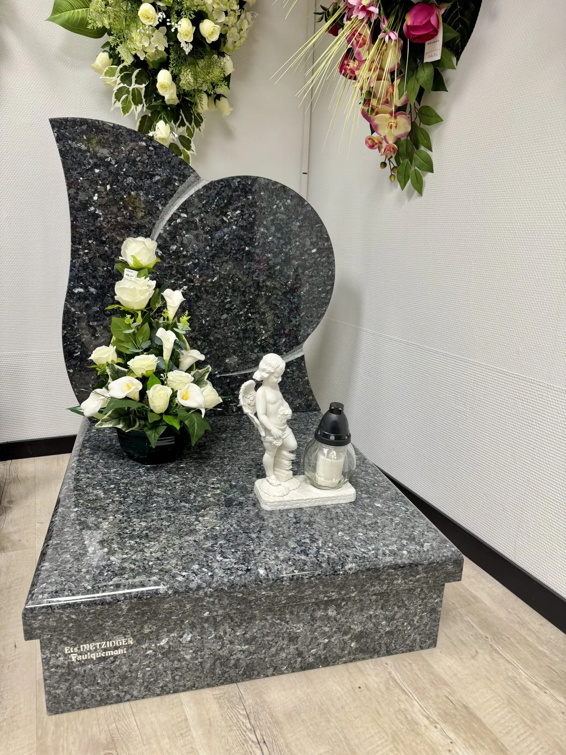 Stèle funéraire sculptée avec statue d'ange et composition de fleurs blanches.