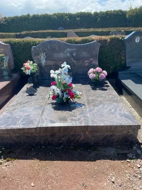 Tombe en granit rose ornée de compositions florales colorées dans un cimetière.