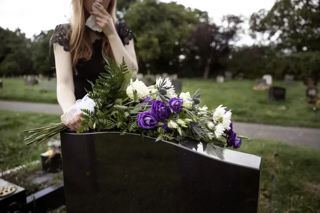 Femme tenant un bouquet de fleurs fraîches posé sur une pierre tombale noire.