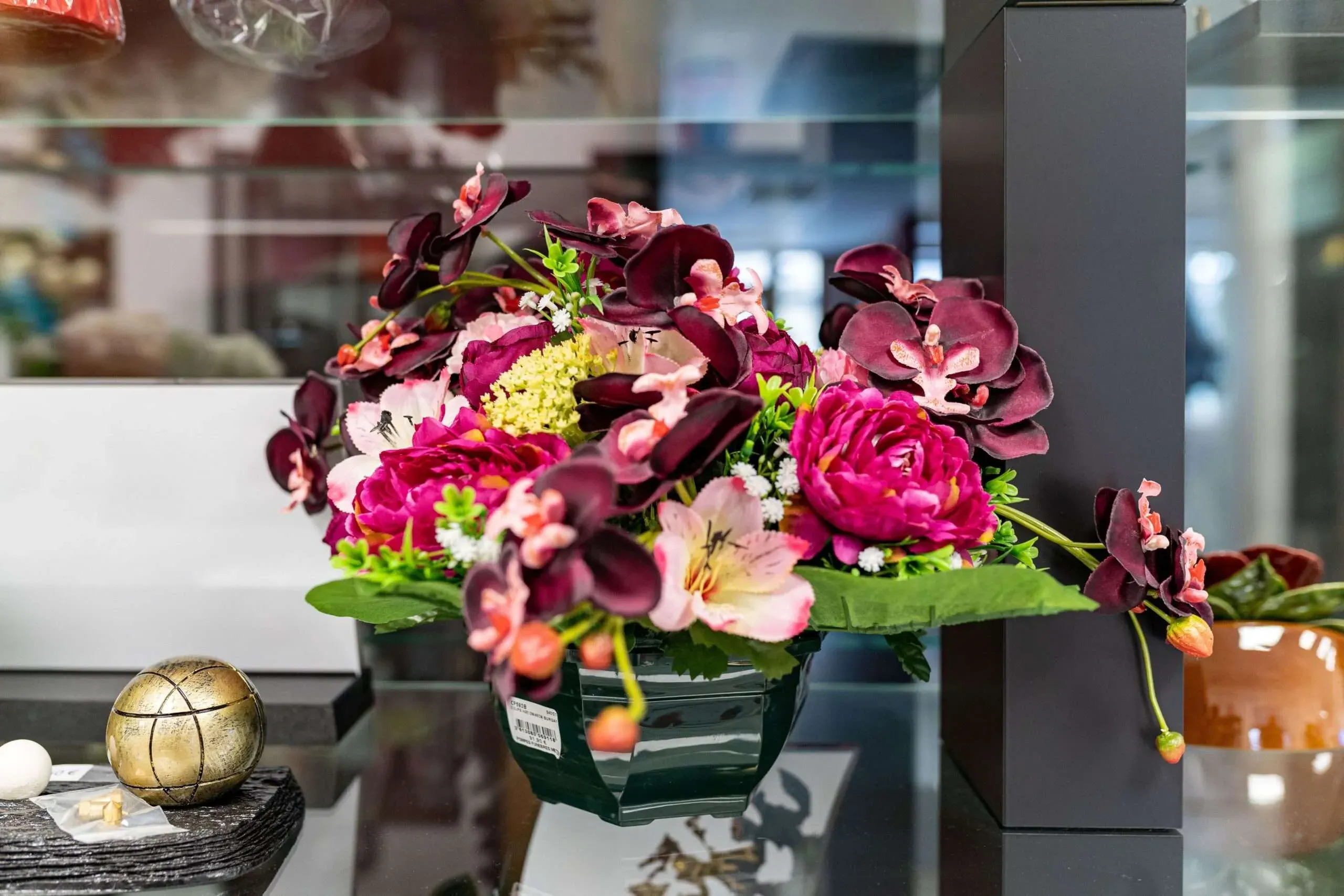 Composition florale artificielle avec orchidées et pivoines roses pour hommage funéraire.