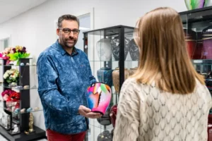 Conseiller funéraire montrant une urne cinéraire colorée à une cliente en magasin.